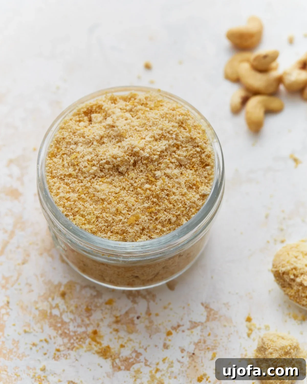 Plant Based Parmesan Perfection 2 A glass jar brimming with homemade vegan parmesan cheese, made from cashews and nutritional yeast, resting on a bright kitchen countertop.