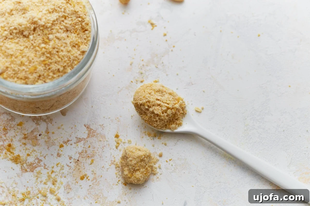 Plant Based Parmesan Perfection 8 A spoonful of finely ground vegan parmesan cheese is held above an open glass jar, against a soft, light background.
