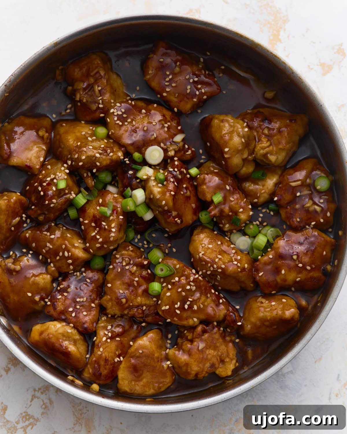 Gluten-free General Tso’s chicken coated in a glossy sweet and spicy sauce, garnished with green onions and sesame seeds in a skillet