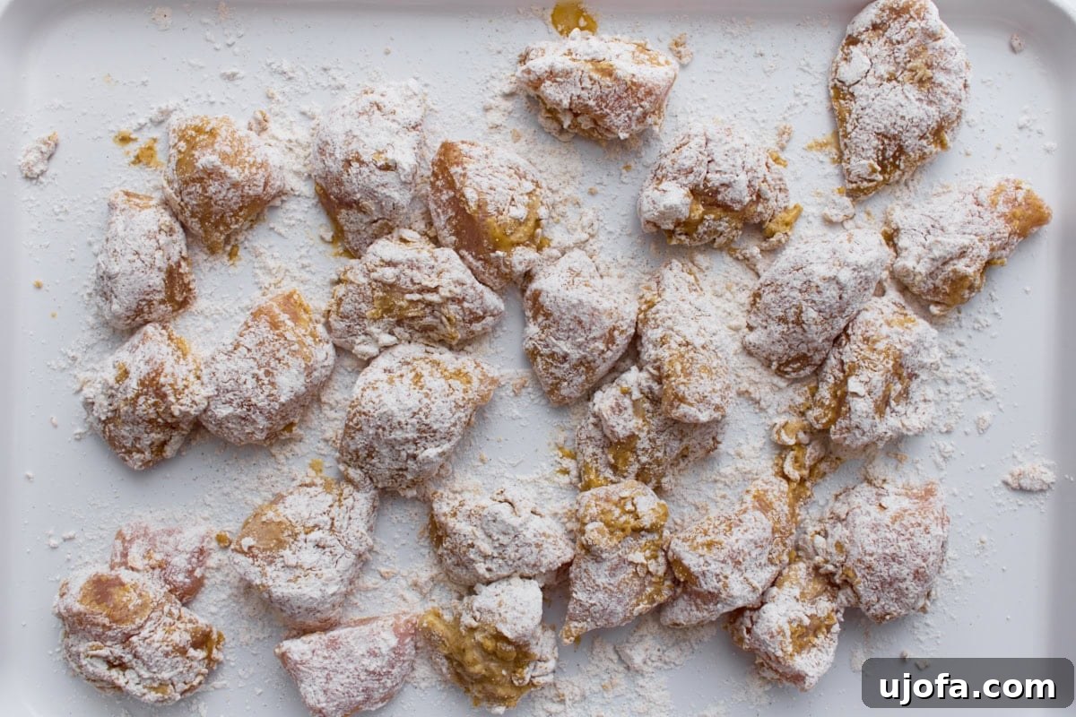 Raw chicken pieces coated in gluten-free flour and cornstarch mixture on a baking sheet