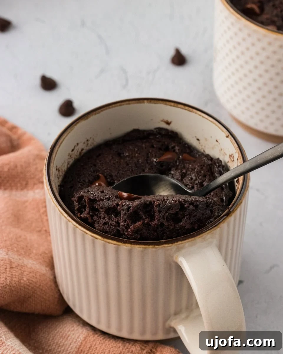 A spoon scooping a generous bite of fudgy almond flour chocolate mug cake from a ceramic mug, revealing melted chocolate chips within its soft, moist interior.