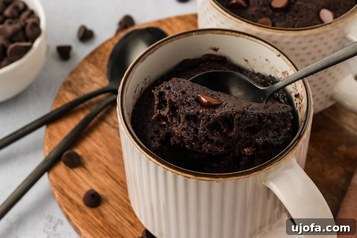 A spoon lifting a soft, moist bite of almond flour chocolate mug cake from a mug, showcasing the rich chocolate texture and delicate crumb.
