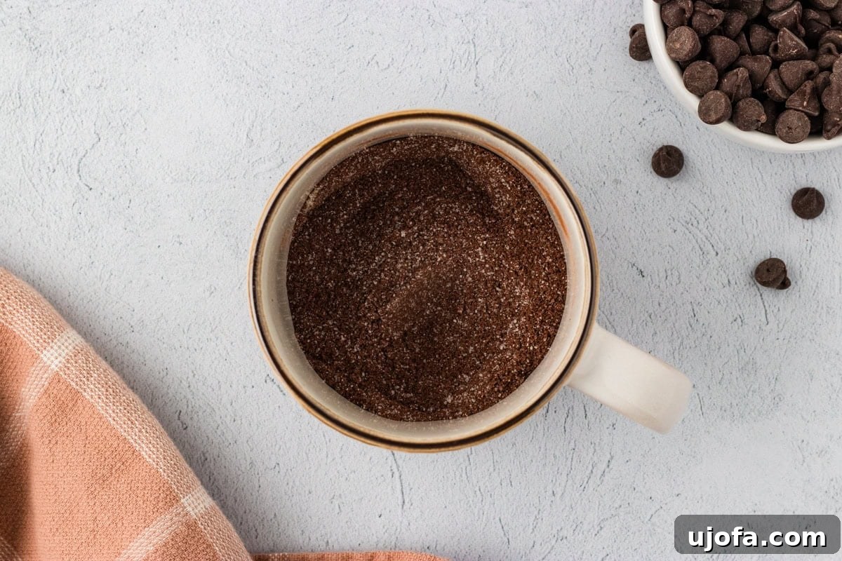 An overhead view of the dry ingredients—almond flour, cocoa powder, sugar, baking powder, and salt—already combined and stirred together in a microwave-safe ceramic mug.