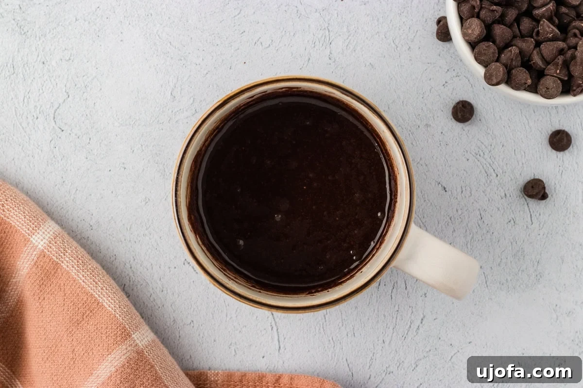 An overhead view of the smooth, glossy, wet batter mixed thoroughly in a mug for almond flour chocolate mug cake, before any chocolate chips are added.