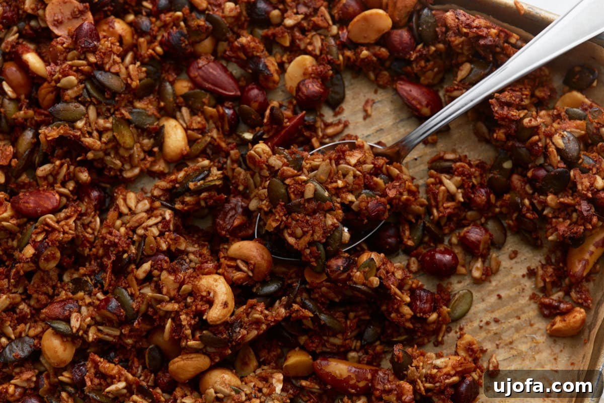 Ketogenic Granola Clusters 10 Spoon scooping chunky keto granola clusters from the baking sheet, highlighting texture and nut variety, ready for serving.