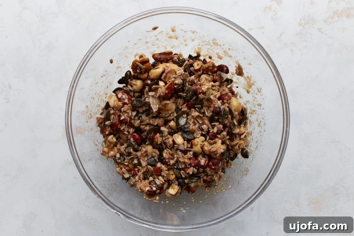 Ketogenic Granola Clusters 6 Keto granola mixture stirred together in a bowl, with nuts and seeds evenly coated in sweetener and oil, showing a glossy finish.
