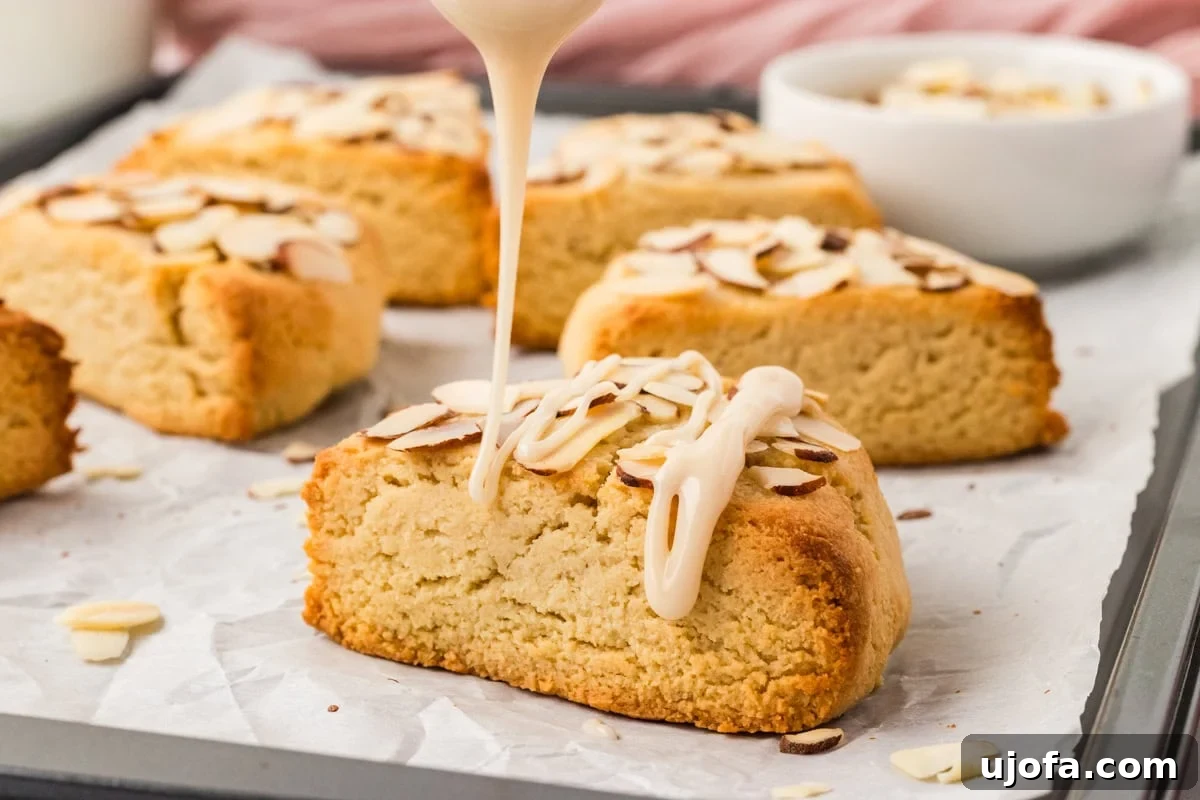 Tender Almond Scones 15 Vanilla icing being drizzled over warm almond flour scone on baking tray