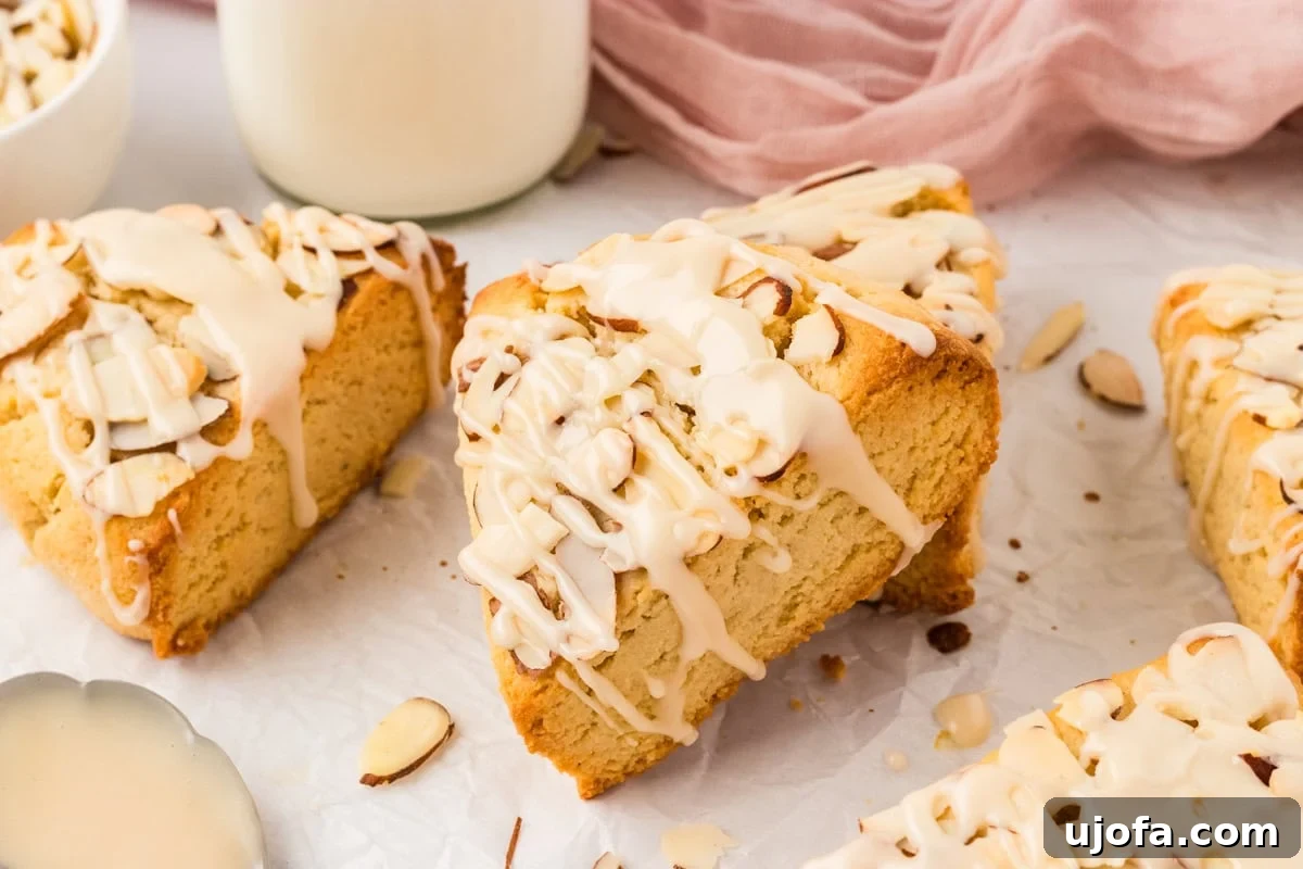 Tender Almond Scones 16 Almond flour scones drizzled with icing and topped with sliced almonds on parchment paper