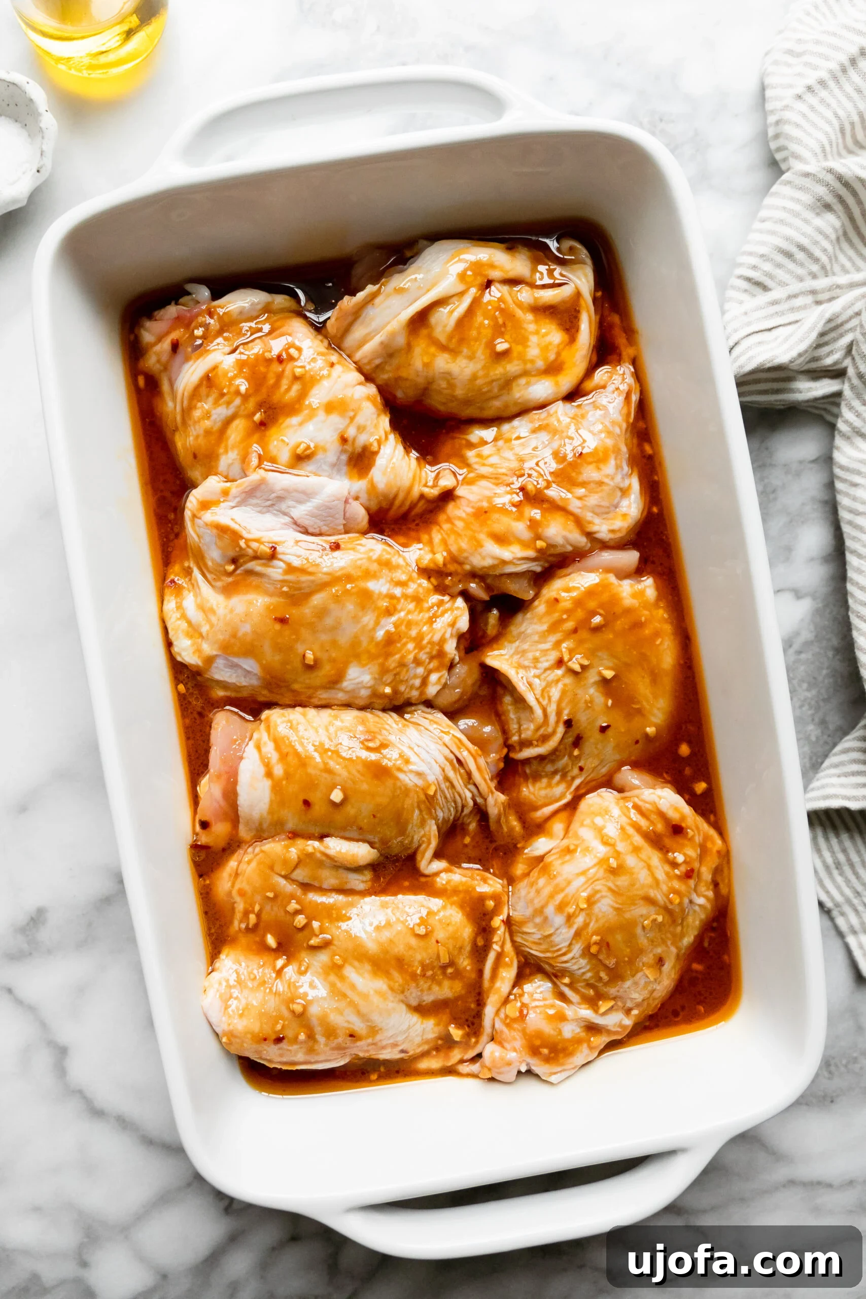 Juicy Keto Chicken Thighs with a Healthy Zesty Marinade 6 A white casserole dish abundantly filled with raw chicken thighs drenched in the savory marinade, ready to be covered and refrigerated.