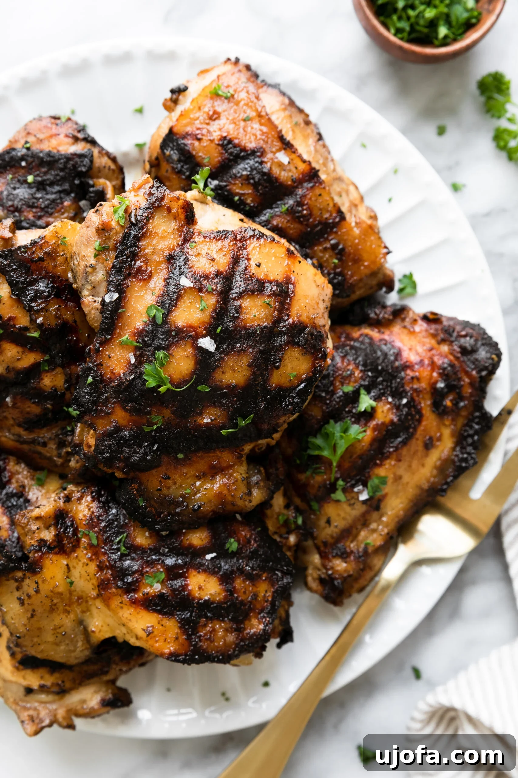 Juicy Keto Chicken Thighs with a Healthy Zesty Marinade 7 Two perfectly grilled marinated chicken thighs on a white plate, served with a gold fork, ready to be enjoyed.