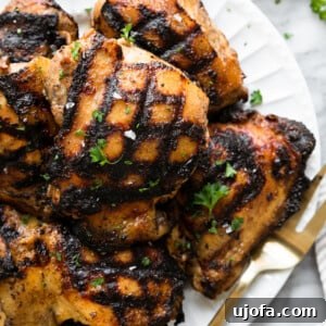 grilled marinated chicken thighs on a white plate with a gold fork