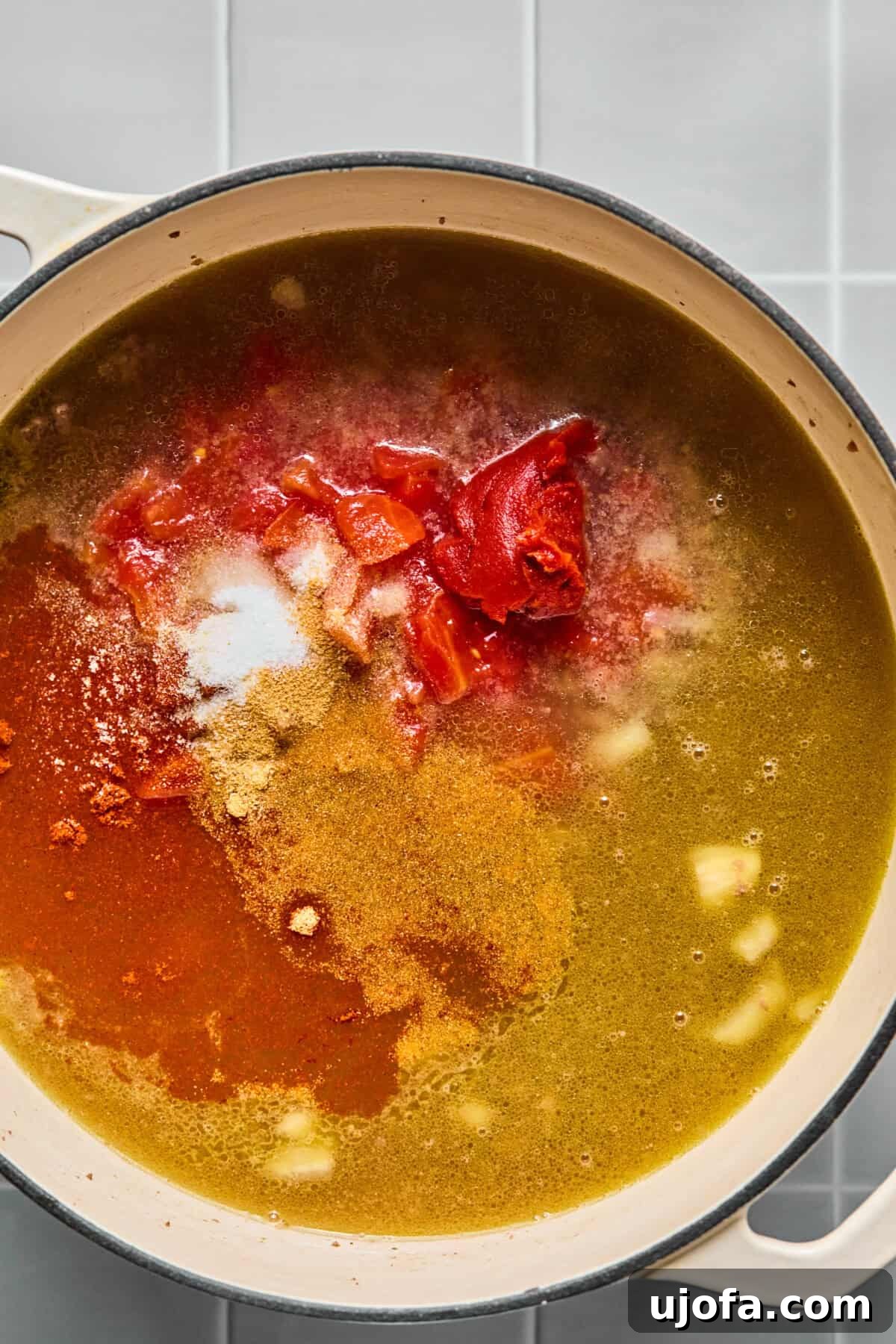 Broth, diced tomatoes, and tomato paste added to the browned beef mixture in a pot.