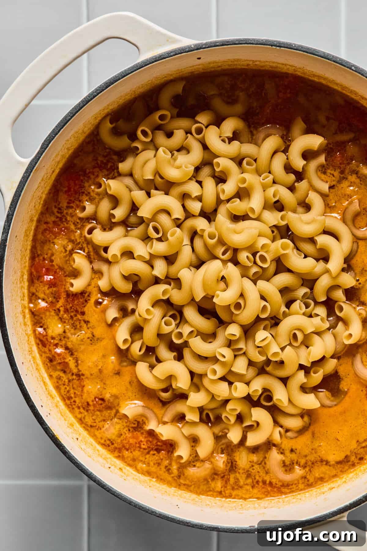 Gluten-free pasta being added to the simmering broth and beef mixture in a pot.