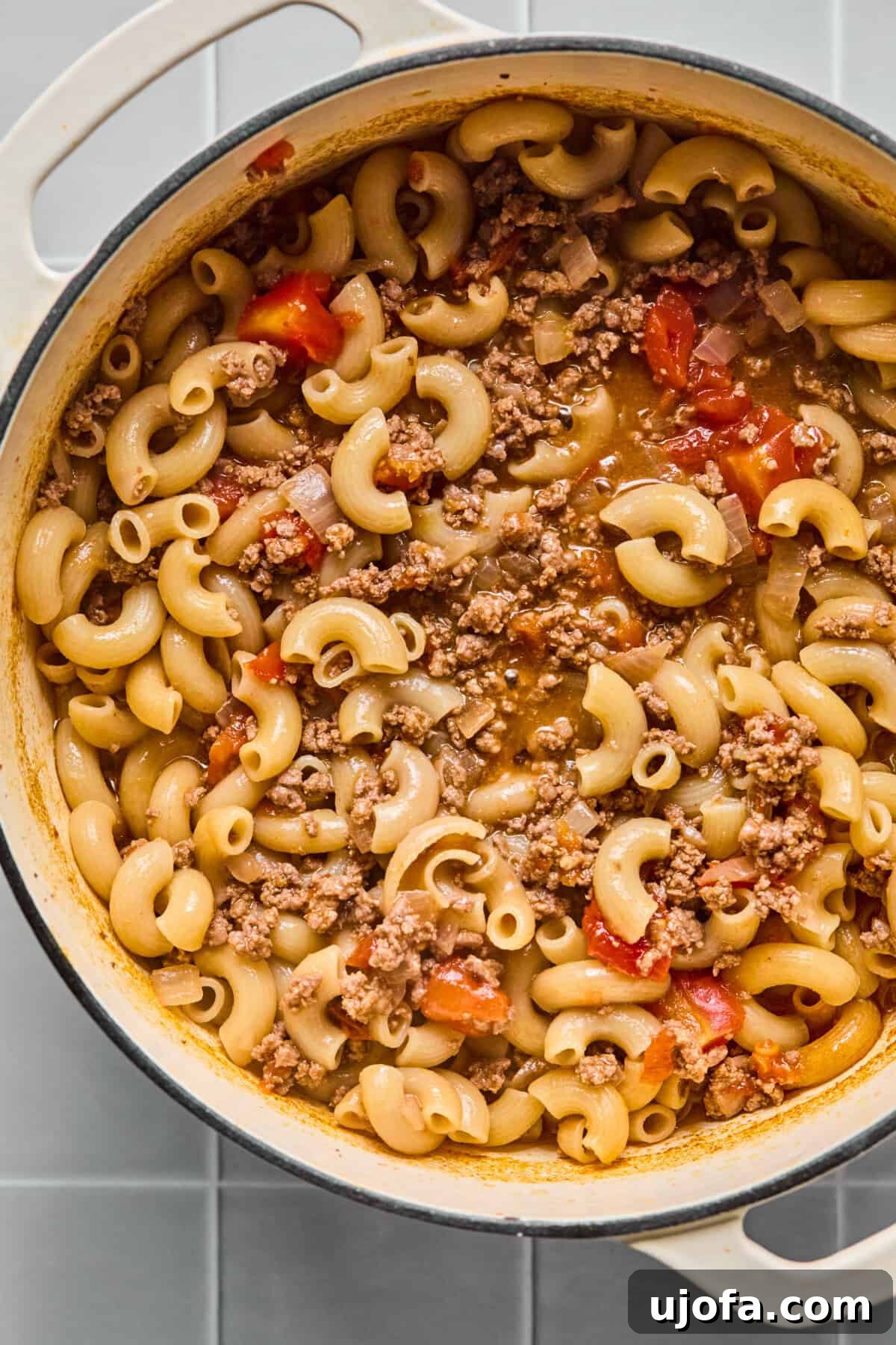 Gluten-free pasta cooking in the pot with ground beef and tomato sauce, absorbing liquid.