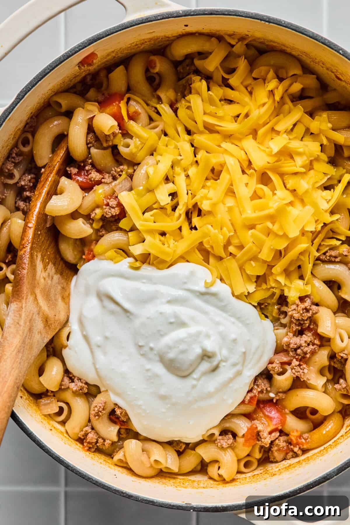 Blended cottage cheese and shredded cheddar being stirred into the finished gluten-free hamburger helper.