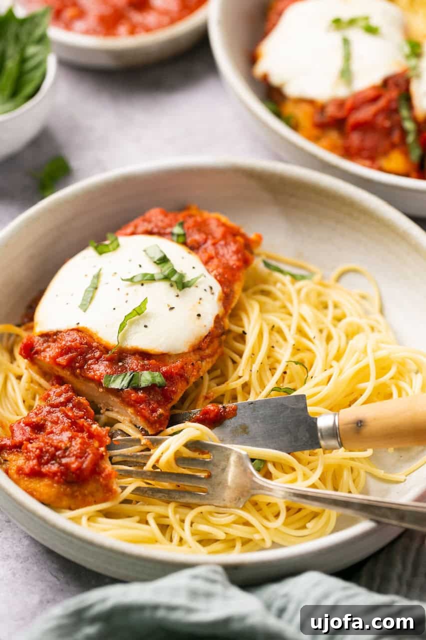 A bowl of spaghetti topped with a chicken parmesan cutlet, being served with a fork and knife.