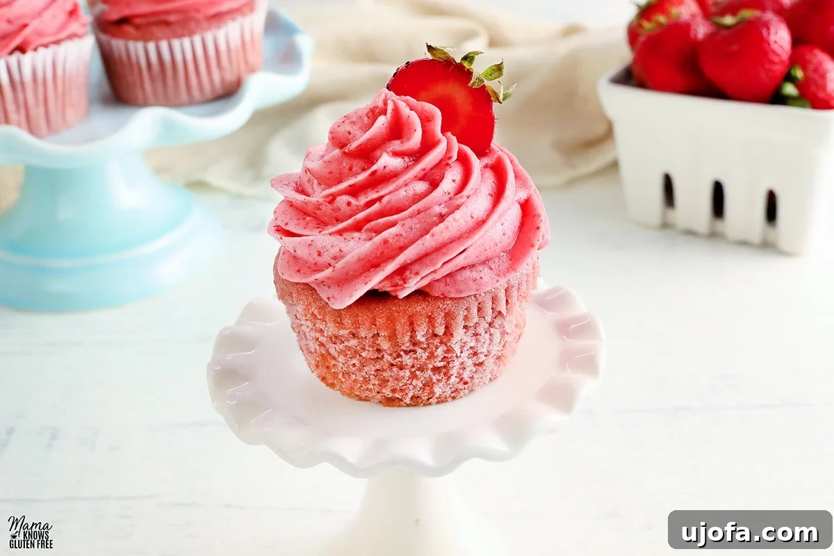 Gluten-free cupcake on a white cupcake stand with cupcakes and strawberries in the background