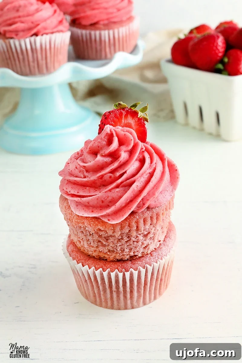 Gluten-free strawberry cupcakes stacked on top of each other with cupcakes and strawberries in the background