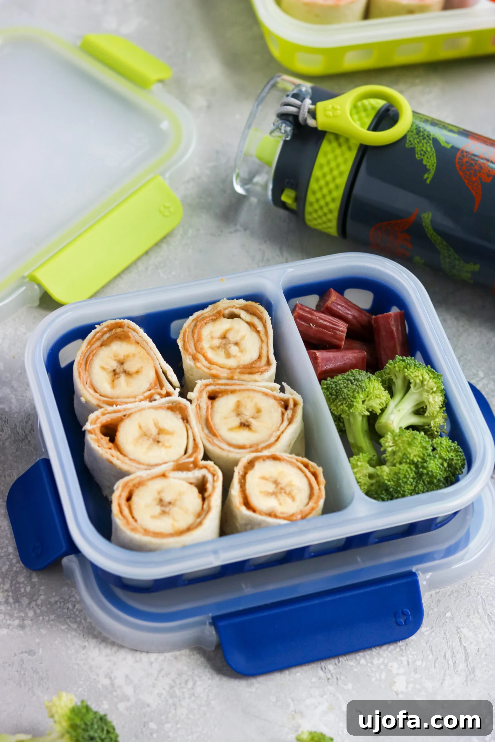 Banana Peanut Butter Honey Pinwheels arranged in a child's lunchbox with a side of beef stick and fresh broccoli florets.