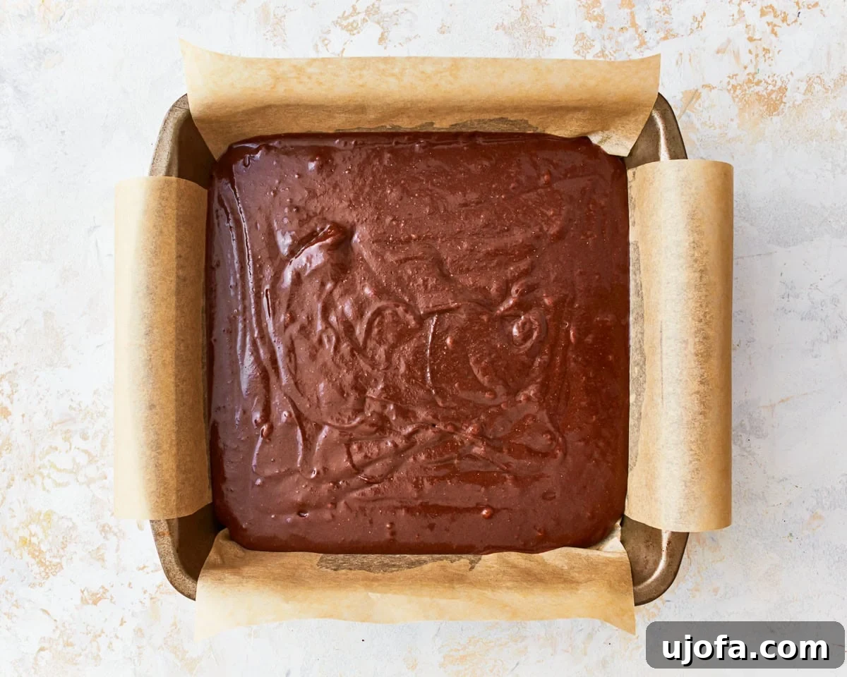 Fudgy Gluten-Free Brownie Perfection 10 Smooth gluten-free brownie batter is poured into a parchment-lined square baking pan, ready for baking.