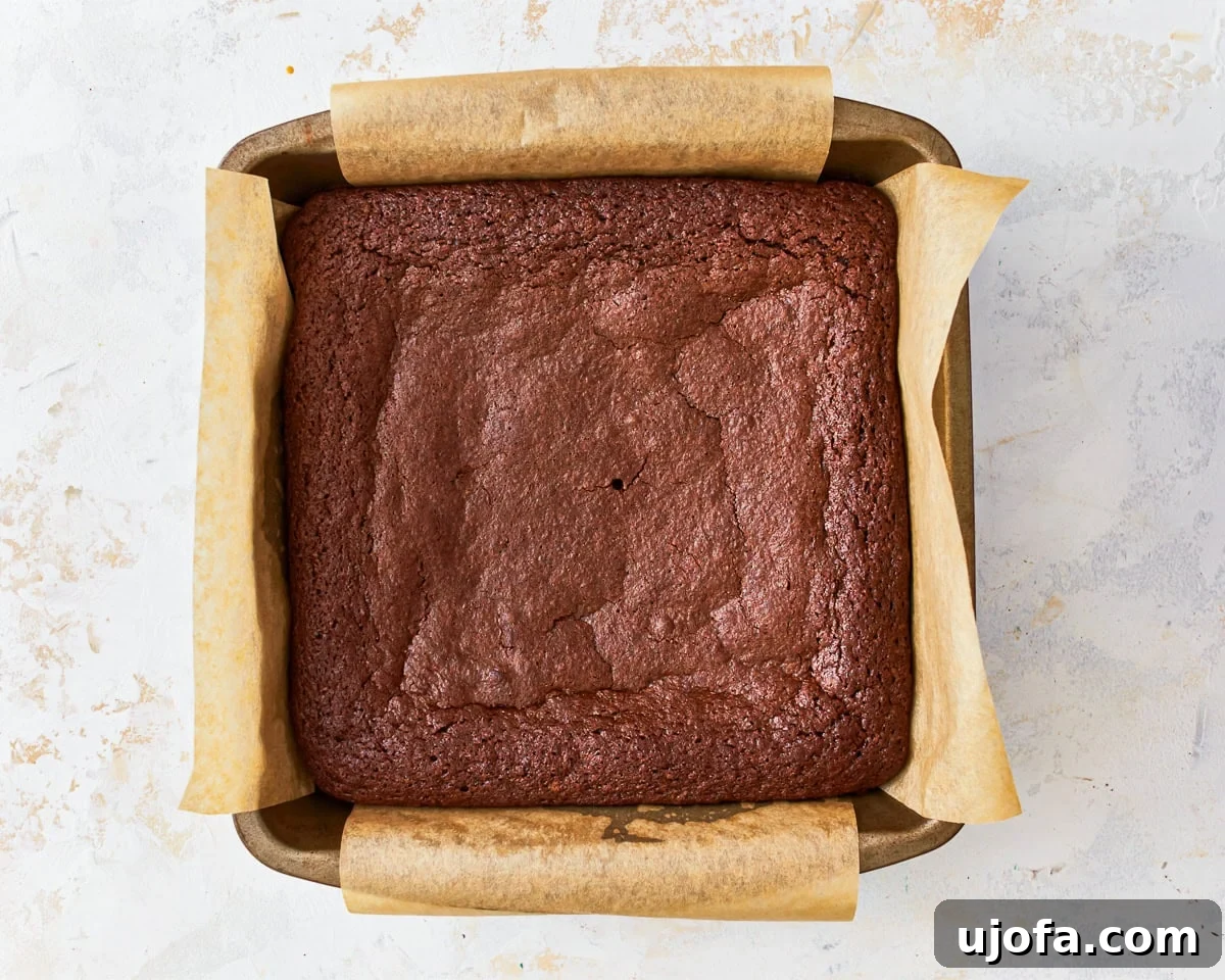 Fudgy Gluten-Free Brownie Perfection 11 Freshly baked gluten-free brownies, still warm in the lined square baking pan, showing a slightly flaky top crust.