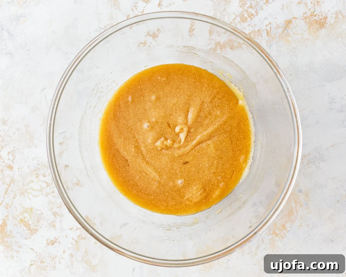 Fudgy Gluten-Free Brownie Perfection 7 Wet ingredients for gluten-free brownies, including melted butter, sugars, and vanilla extract, are being mixed in a clear glass bowl.