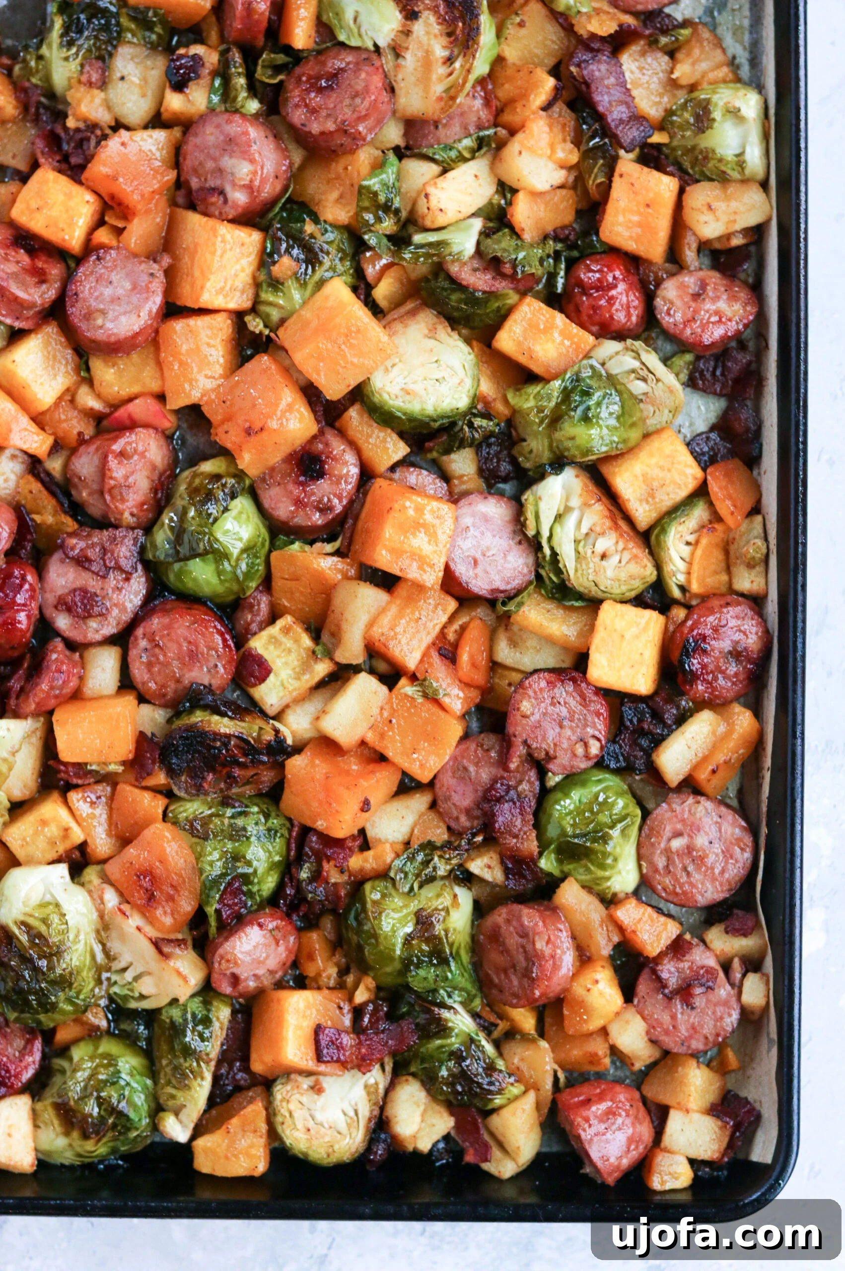 A beautifully arranged Whole30 Harvest Sheet Pan Dinner with chicken sausage, apples, butternut squash, Brussels sprouts, and bacon, ready to be baked.