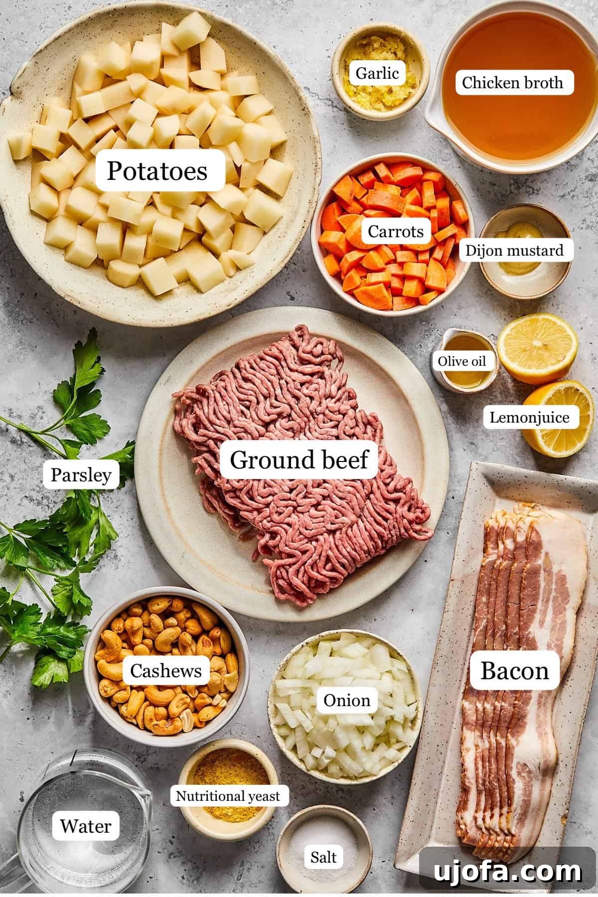 Creamy Dairy-Free Bacon Cheeseburger Soup 3 A collection of fresh ingredients for cheeseburger soup, including diced onions, carrots, garlic, raw cashews, and potatoes, arranged in nesting bowls.