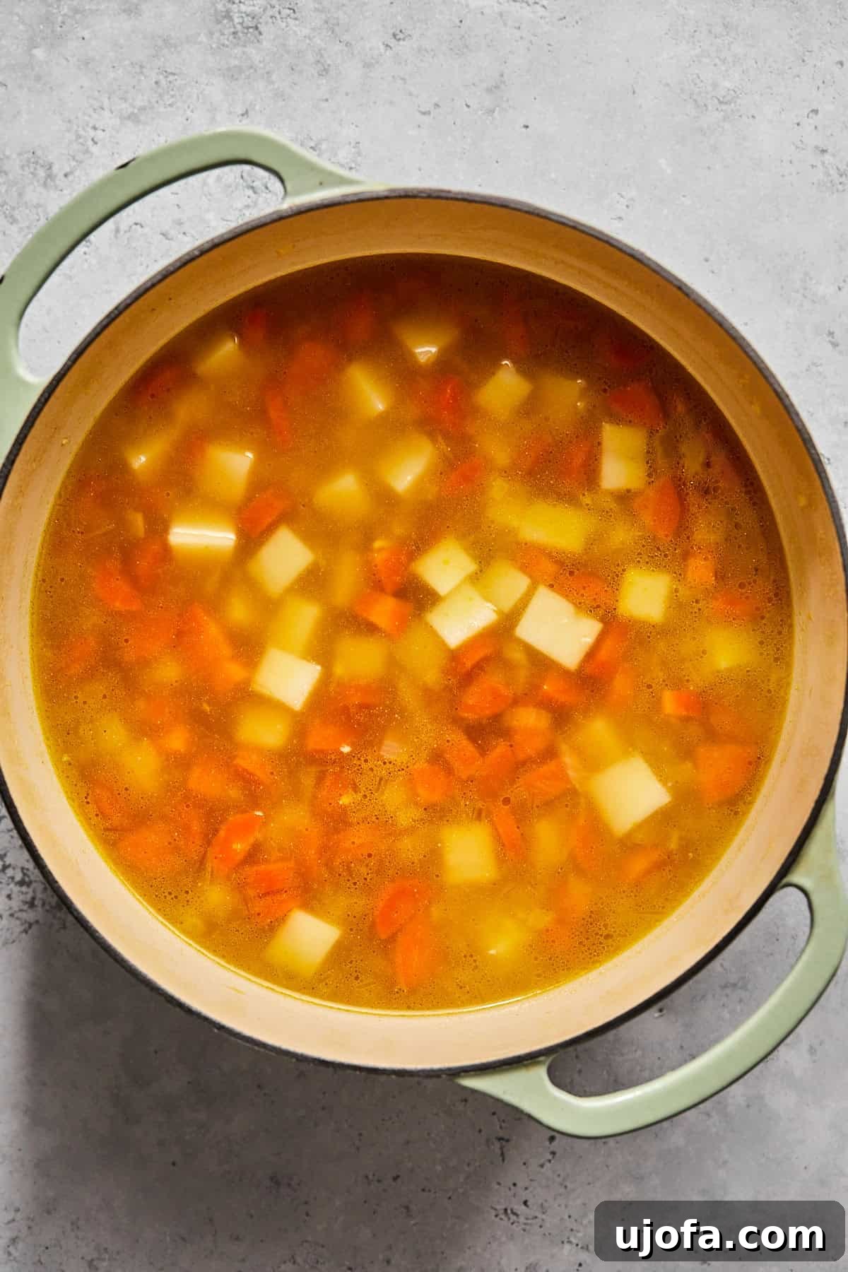 Creamy Dairy-Free Bacon Cheeseburger Soup 7 Potatoes, carrots, and chicken broth simmering together in a pot, creating the soup base.