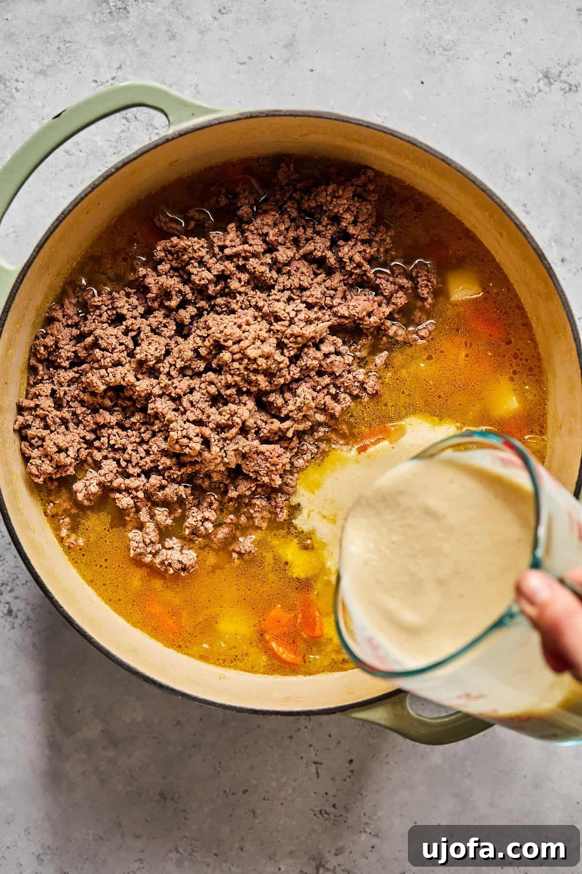 Creamy Dairy-Free Bacon Cheeseburger Soup 9 The blended cashew cheese sauce being poured into a pot containing ground beef and broth, mixing into the soup base.
