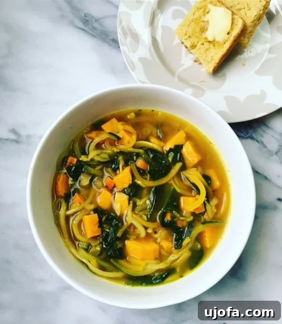 Vibrant Zoodle Vegetable Soup 2 A vibrant bowl of Veggie Loaded Zoodle Soup with fresh herbs on top, beside a piece of cornbread.
