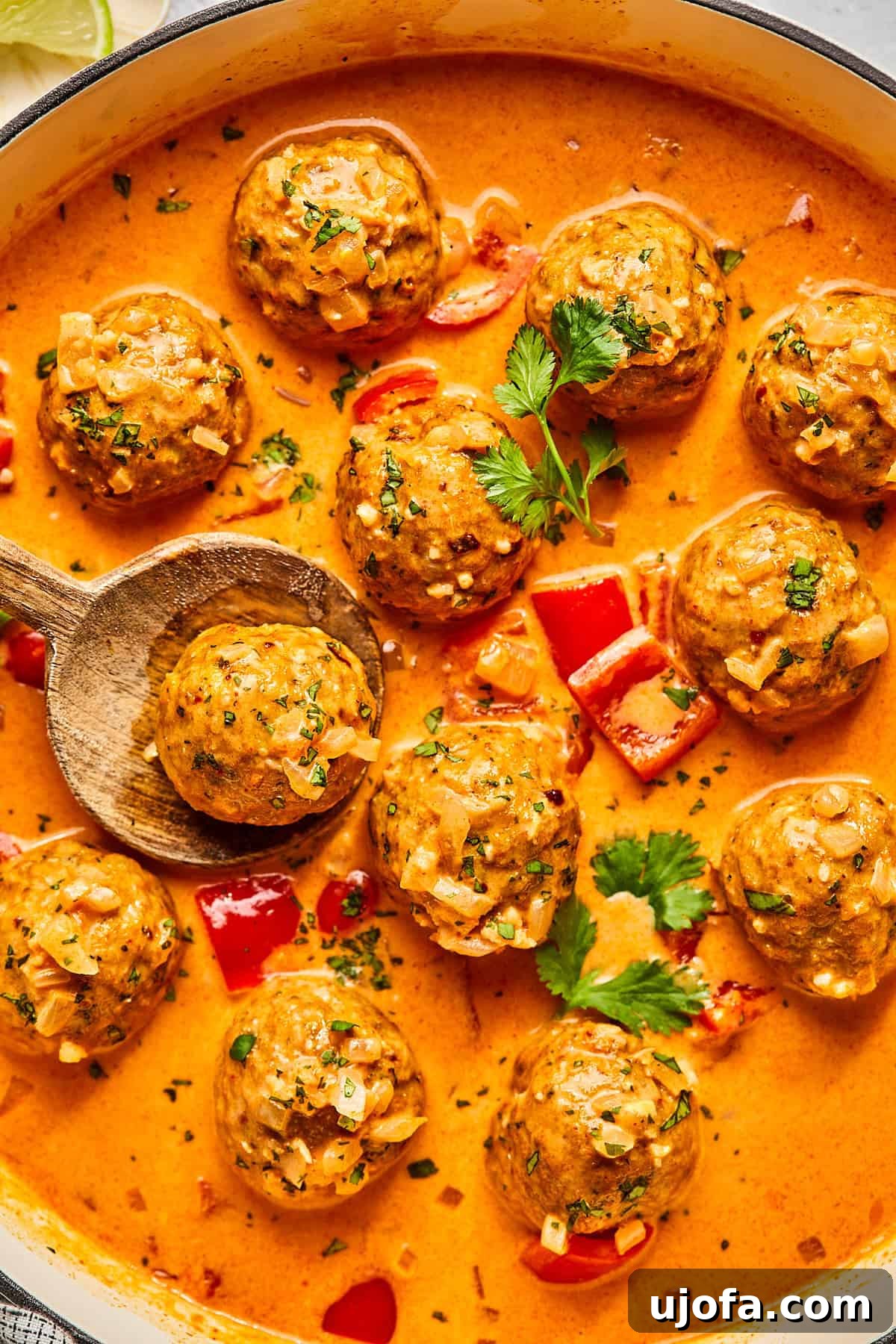 Thai Turkey Meatballs in red curry sauce in a skillet with a spoon lifting one of the meatballs