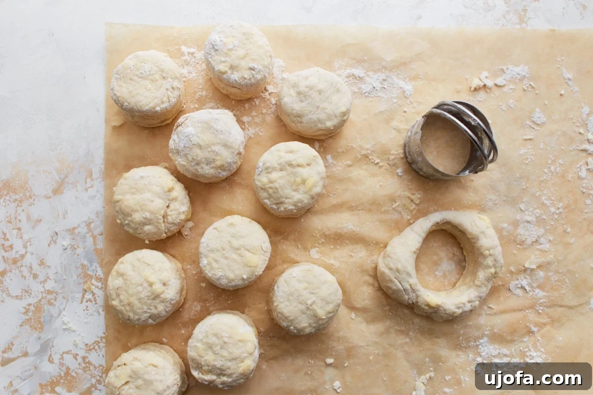Perfect Gluten-Free Buttermilk Biscuits 13 Unbaked gluten-free biscuit rounds cut from the dough, placed on parchment paper, with a biscuit cutter nearby.