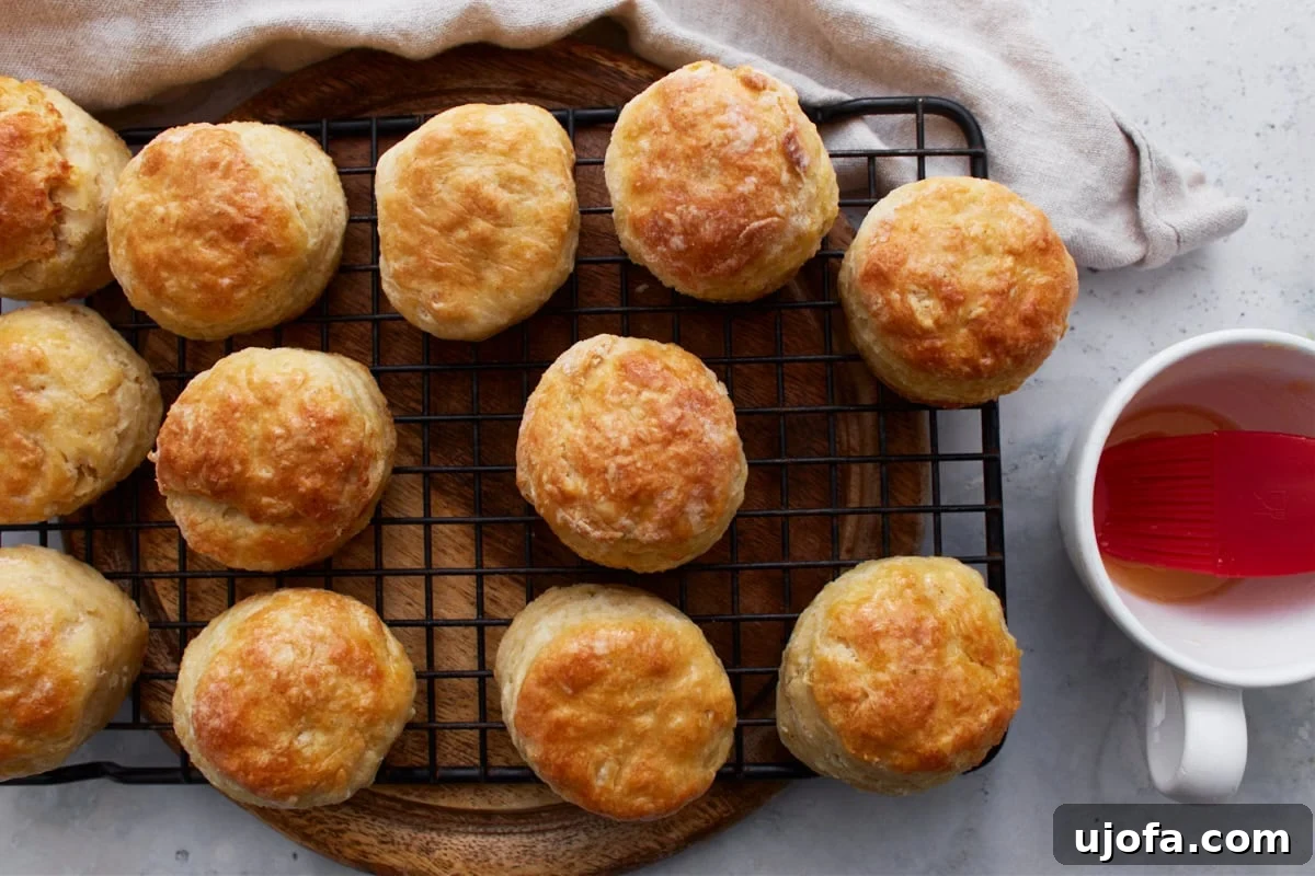 Perfect Gluten-Free Buttermilk Biscuits 16 Warm, baked gluten-free biscuits on a wire rack, with a pastry brush and a small bowl of melted butter nearby.