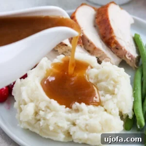 Rich Paleo Gravy being generously poured over a serving of mashed potatoes, with turkey in the background