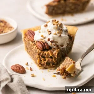 Gluten-free pecan pie slice on a plate, topped with whipped cream, with a fork taking a bite