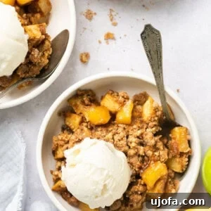 Warm Healthy Apple Crumble topped with a scoop of ice cream and a spoon, served in a white bowl