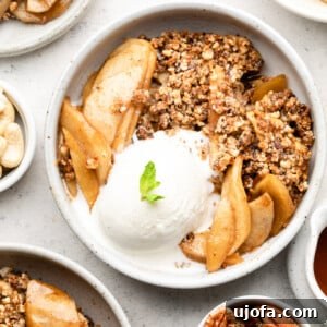 Warm Paleo Apple Crisp in a white bowl, topped with ice cream and a sprig of mint