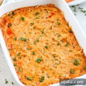 Healthy buffalo chicken dip in a white baking dish topped with fresh parsley, served with carrots and celery sticks