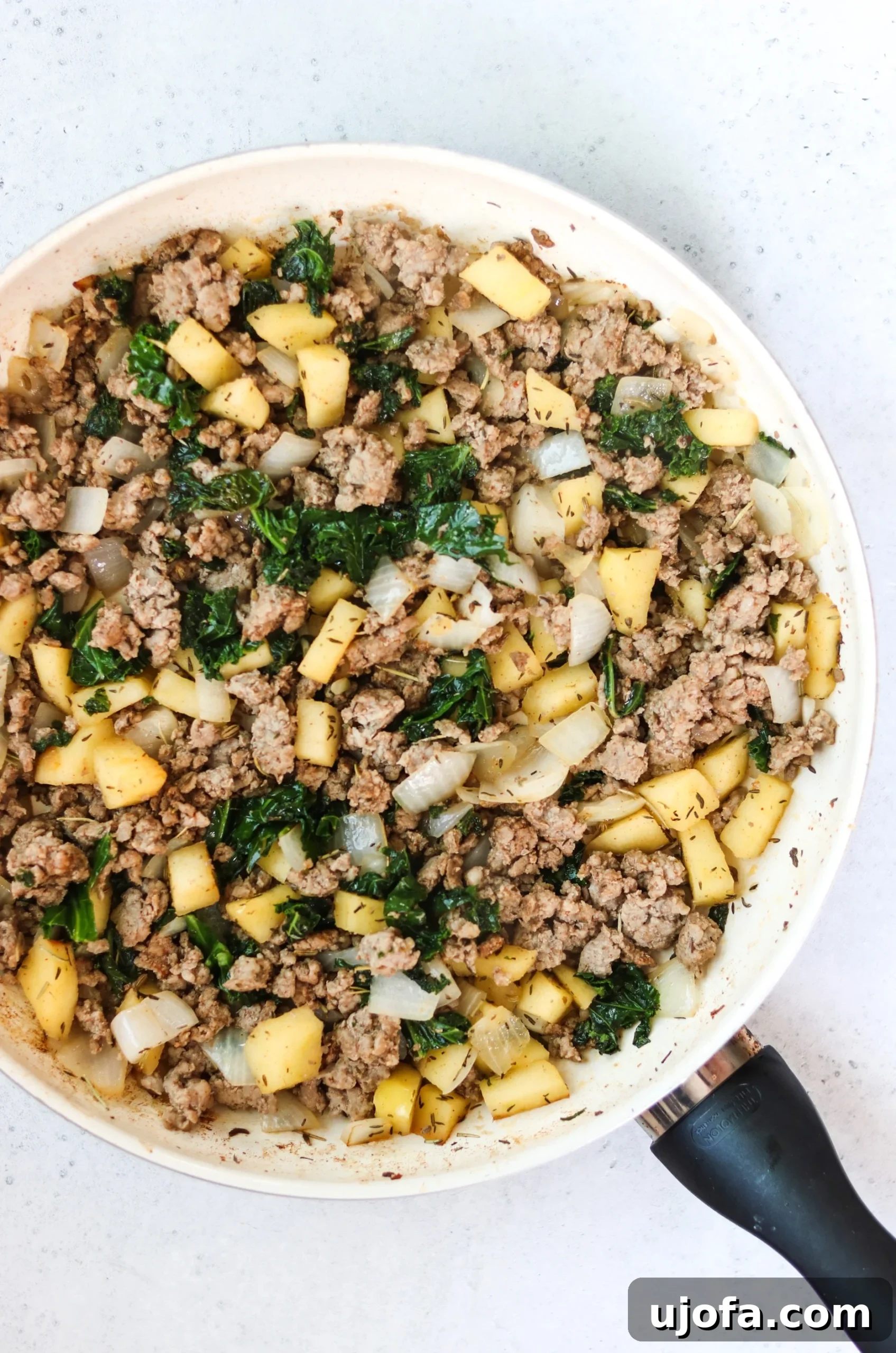 Golden Acorn Harvest Bowls 6 A close-up of the prepared filling for the acorn squash, showing cooked pork sausage, kale, apples, and onions simmering in a pan.