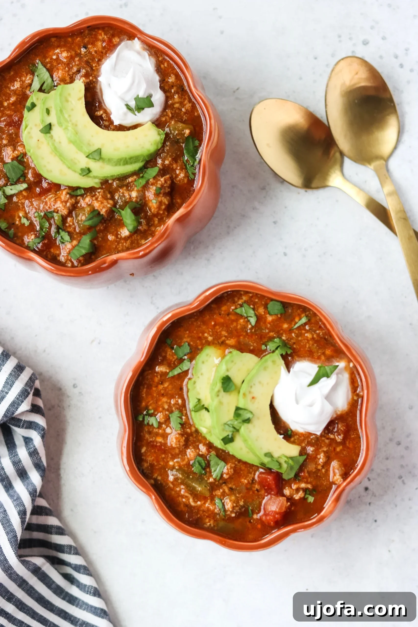 A top-down view of Instant Pot Pumpkin Turkey Chili served in a rustic pumpkin-shaped bowl, garnished with fresh cilantro and a dollop of coconut cream.