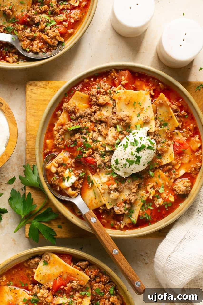 Three bowls of vibrant gluten-free lasagna soup, each topped with a dollop of creamy dairy-free ricotta cheese and fresh parsley.