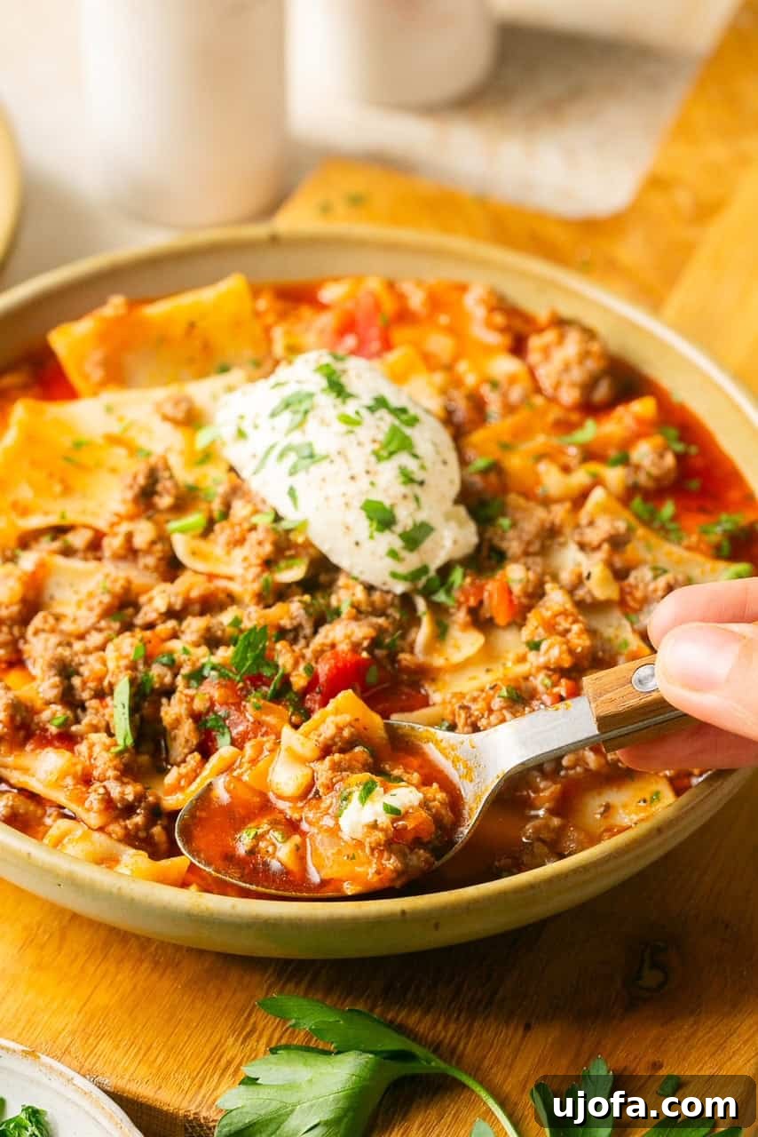 A close-up shot of a spoon brimming with gluten-free lasagna soup, showing tender noodles, meat, and rich tomato broth.
