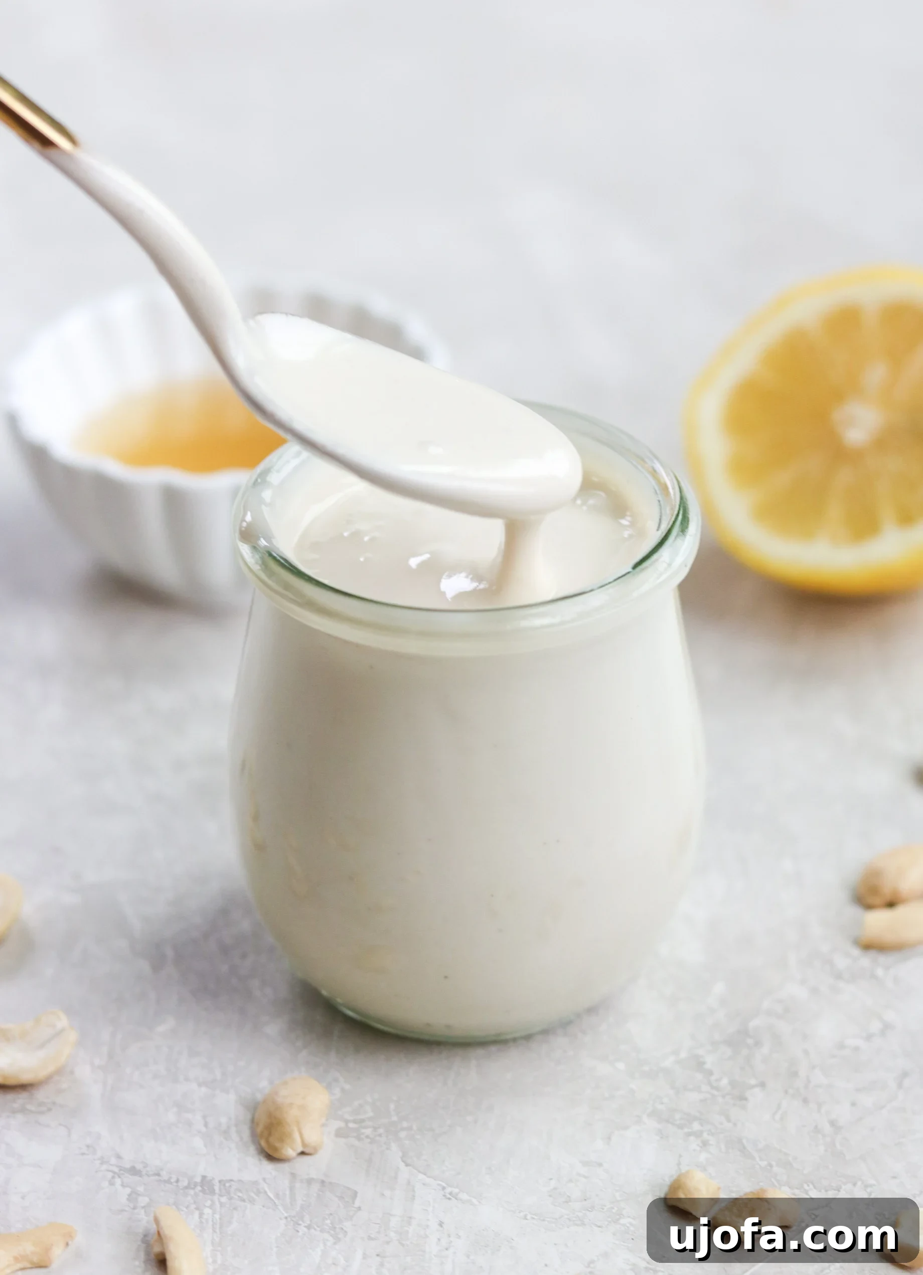 A gold spoon lifting creamy homemade dairy-free sour cream out of a glass jar, showcasing its smooth texture.