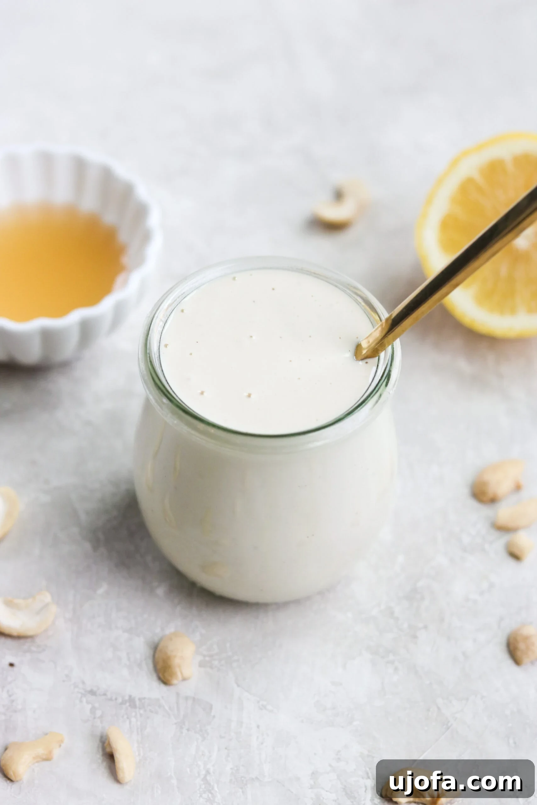 A jar of smooth vegan paleo dairy-free sour cream with cashews sprinkled on top, beside a small bowl of apple cider vinegar and a lemon half, highlighting the fresh ingredients.