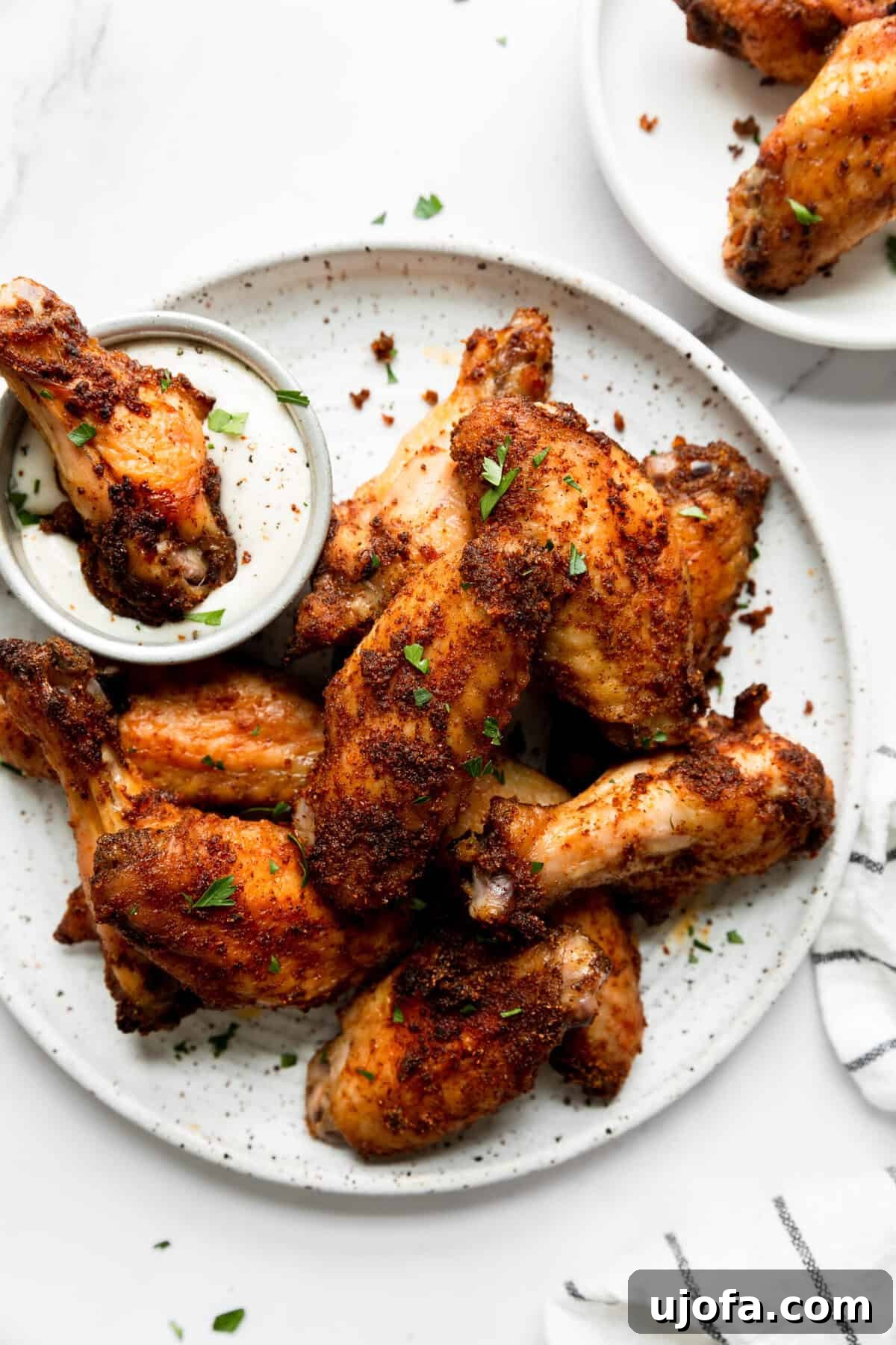 Crispy dry-rubbed baked chicken wings served on a white plate, with one wing being dipped in creamy ranch dressing.