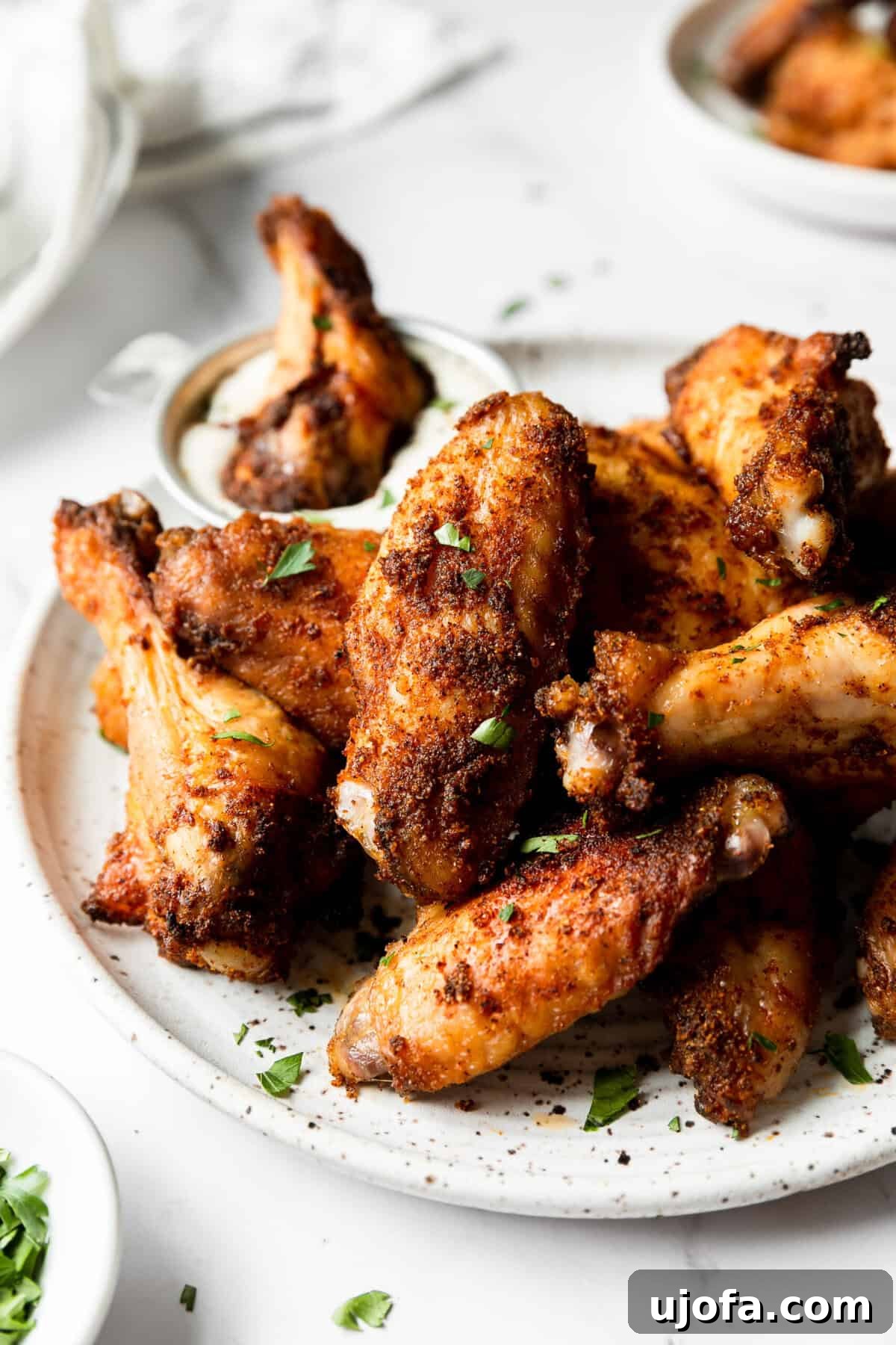 A close-up shot of dry-rubbed baked chicken wings on a plate, with one wing being dipped into a small bowl of ranch dressing.