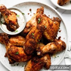 Dry rubbed baked chicken wings on a white plate with one being dipped in ranch dressing