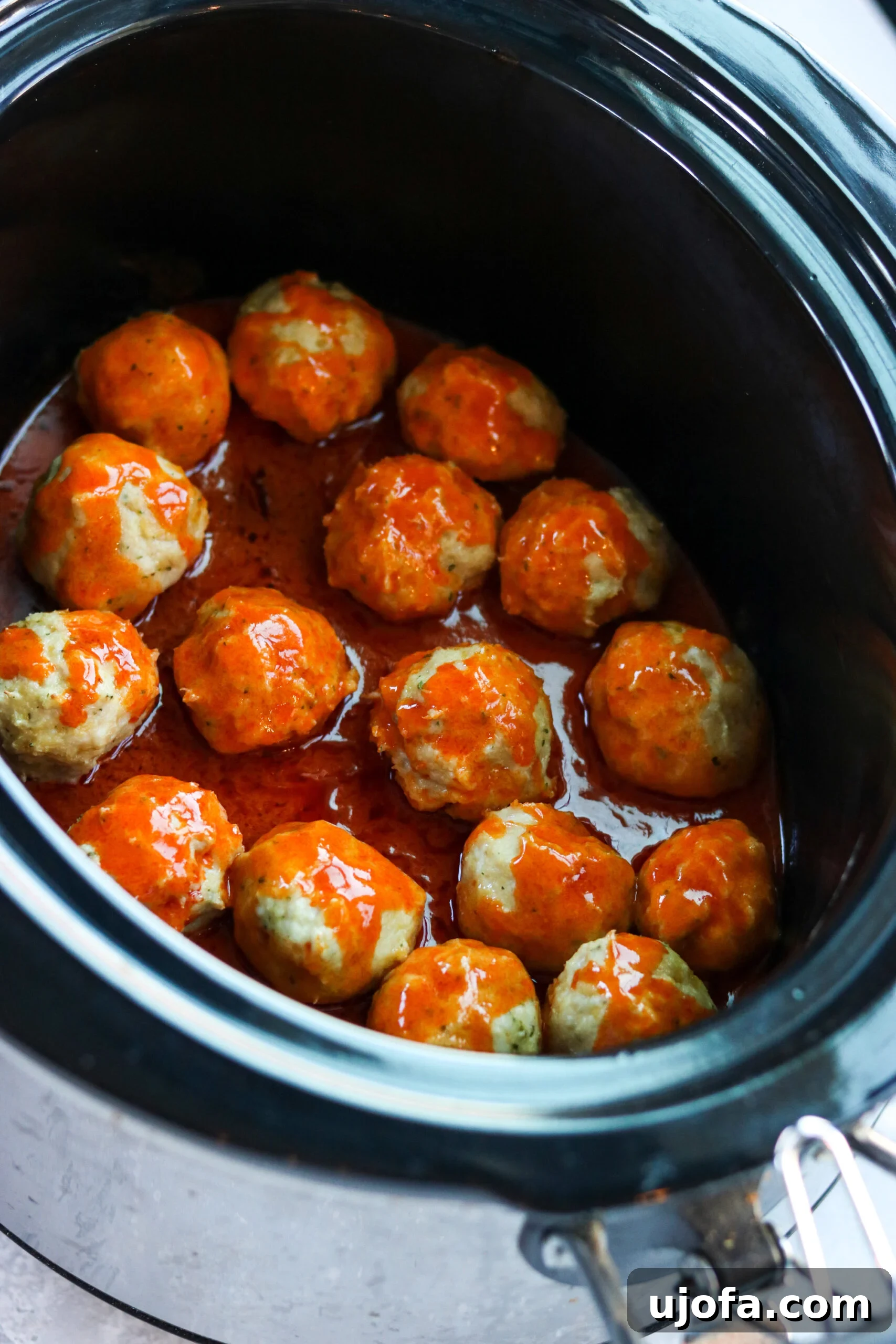 A slow cooker filled with saucy buffalo chicken meatballs, garnished with fresh cilantro, indicating a ready-to-serve, gluten-free dish.