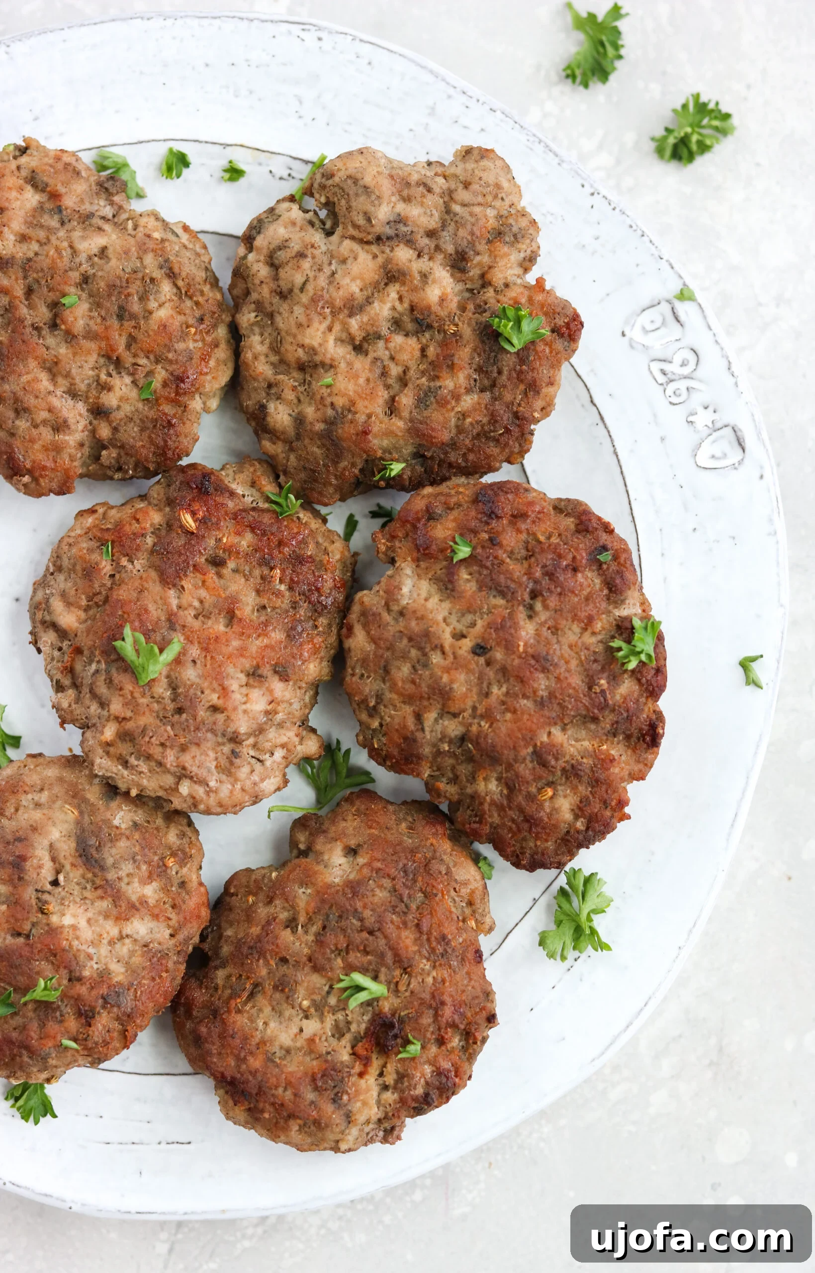 Freshly cooked Air Fryer sausage patties on a white plate, garnished with vibrant green parsley.